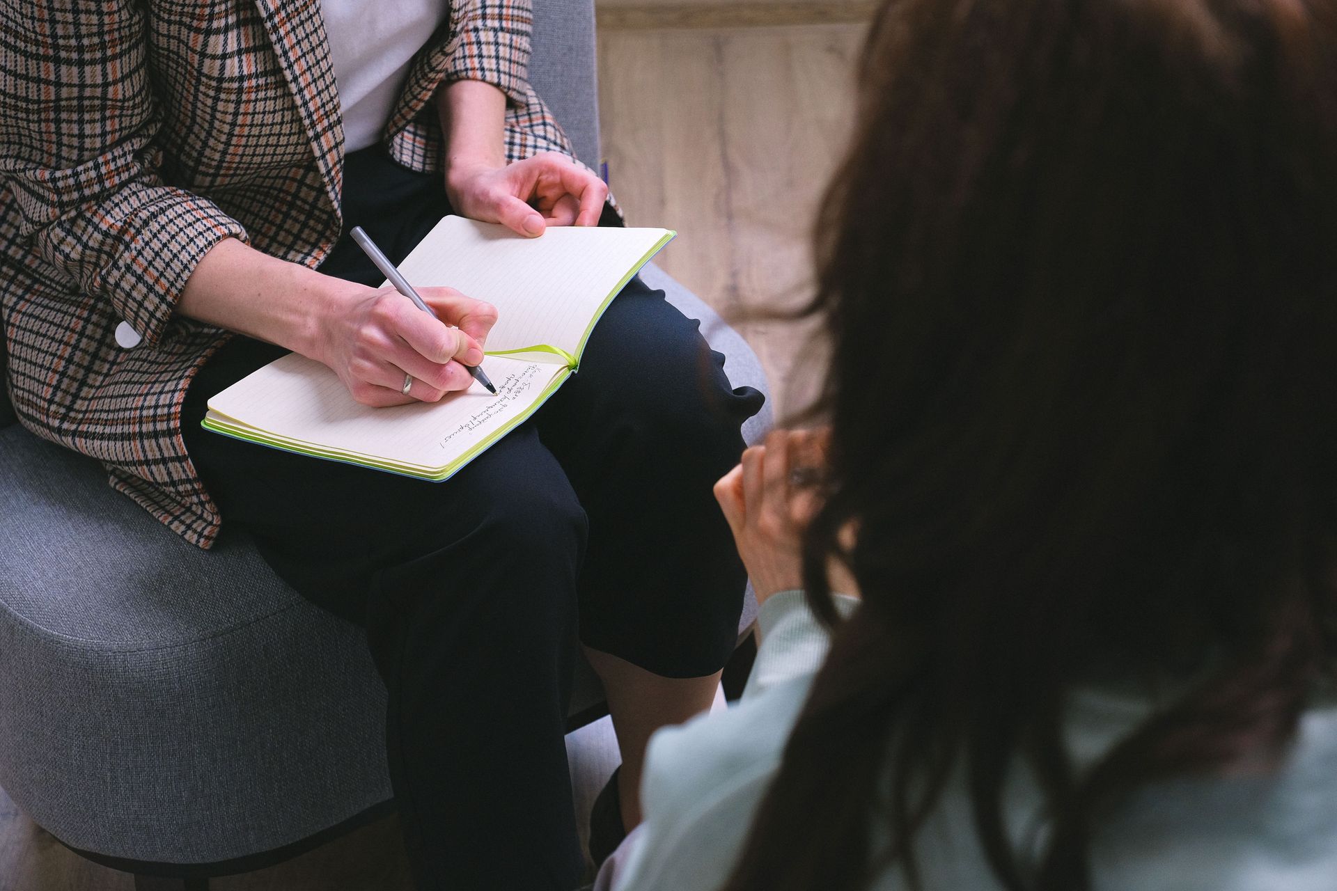 From above of crop anonymous psychotherapist taking notes in agenda while speaking with woman during psychological session