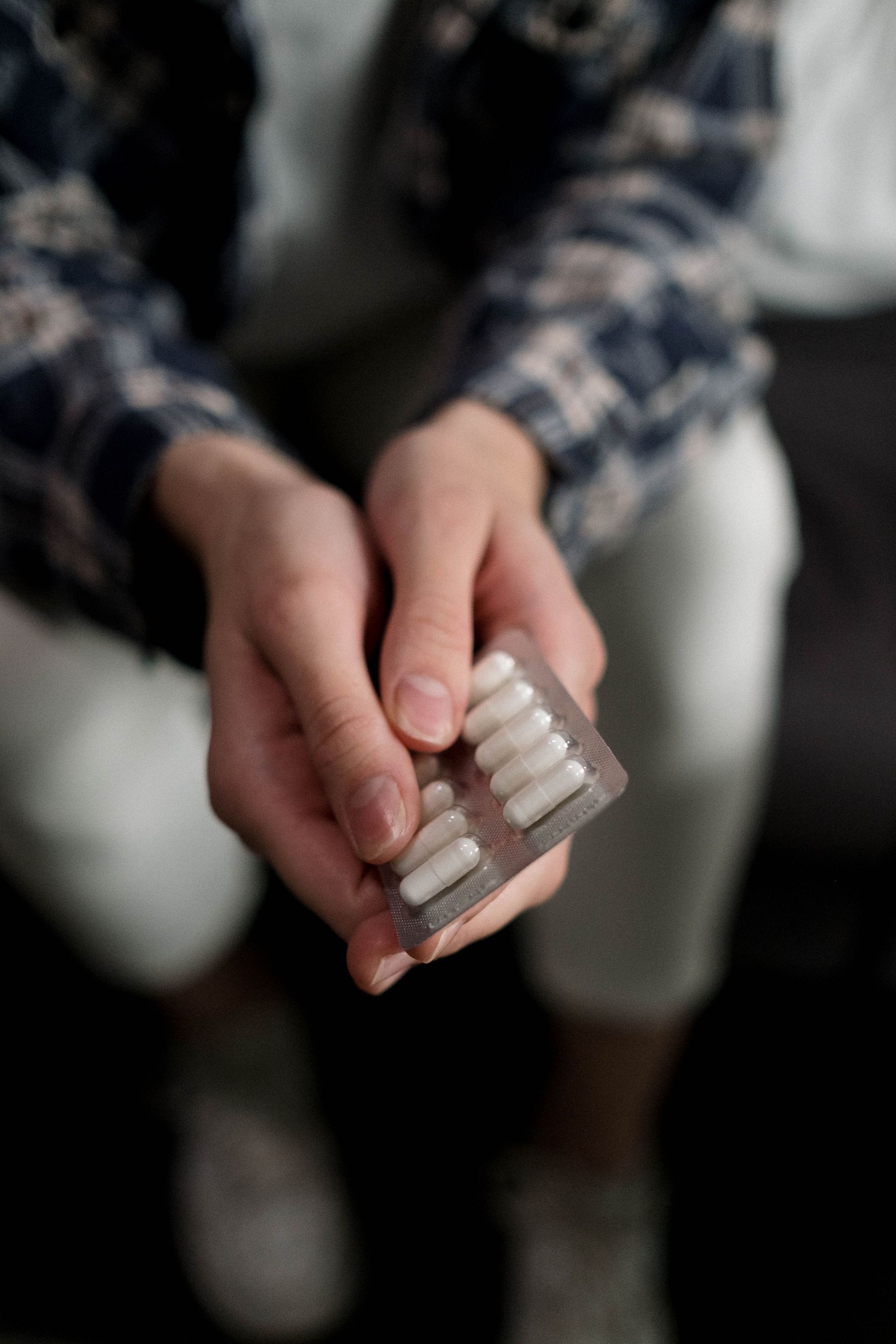 Close-up of hands holding a blister pack of white capsules, emphasizing medication and health.