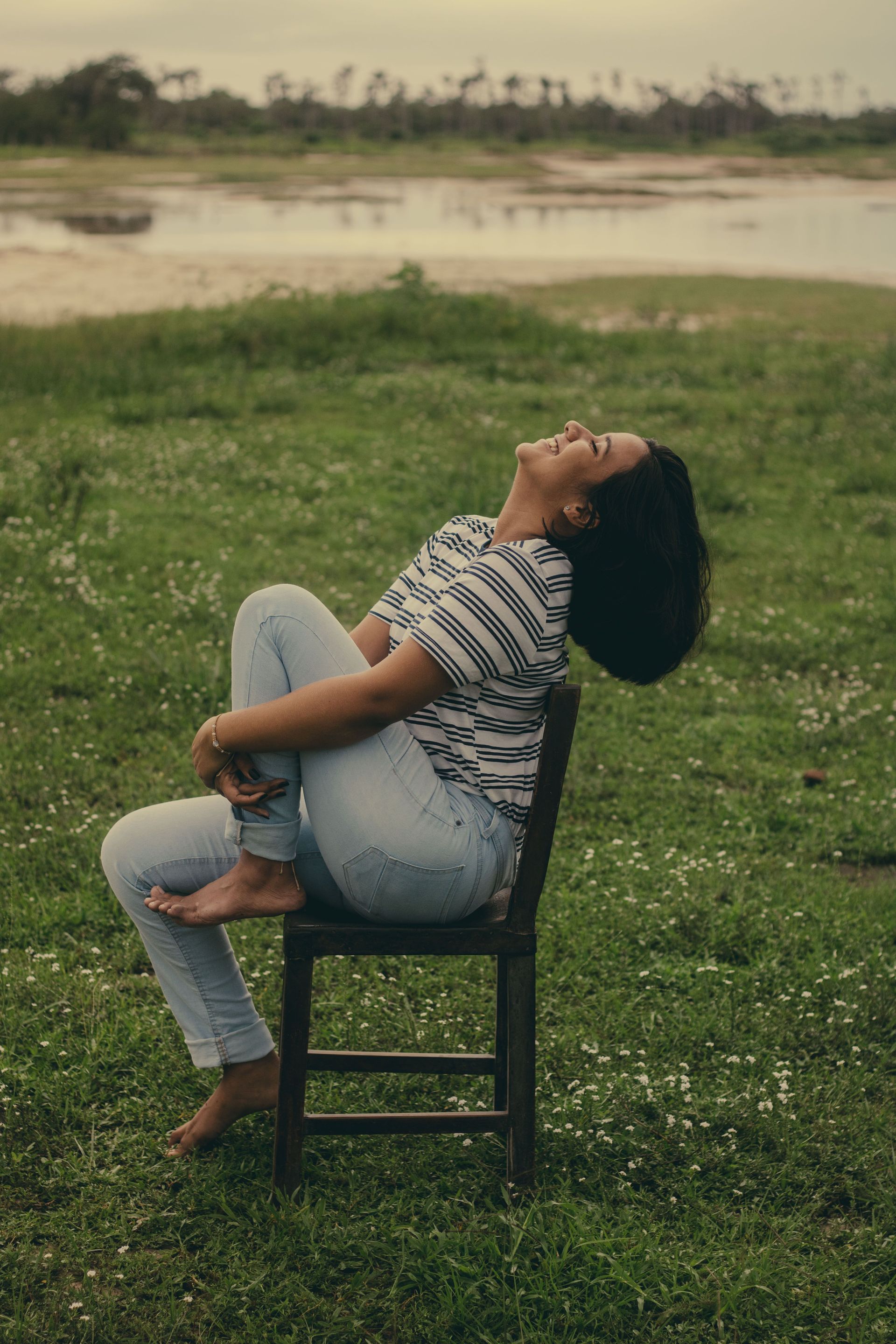 A happy woman sits relaxed on a chair outdoors, embracing nature and leisure.